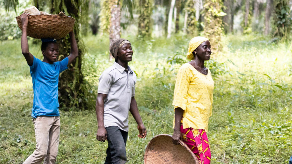 Lucia Mansaray, cocoa farmer from Sierra Leone walking with son Beshey and cocoa farm helper at the edge of the Gola Rainforest