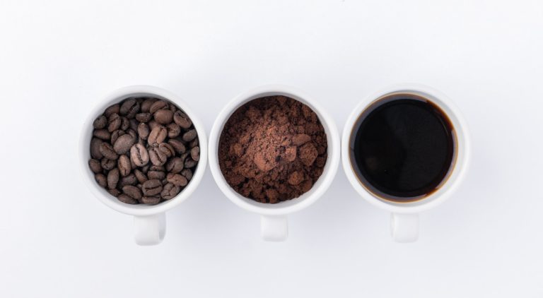 Three cups, one with coffee beans, second with ground coffee and the third with a coffee drink